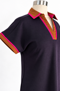 A short-sleeve polo shirt dress on a mannequin, featuring a dark navy body with a contrasting brown collar and sleeve cuffs, trimmed with bright pink piping.