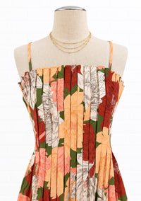 A sleeveless floral dress displayed on a cream fabric mannequin torso against a white brick wall. 