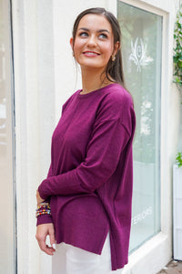 Model is wearing a burgundy long sleeve top with white jeans on a downtown street.