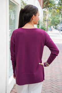Model is wearing a burgundy long sleeve top with white jeans on a downtown street.