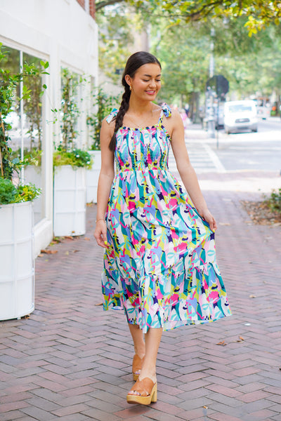 Model is wearing a colorful abstract print midi dress with brown heels on a downtown street.