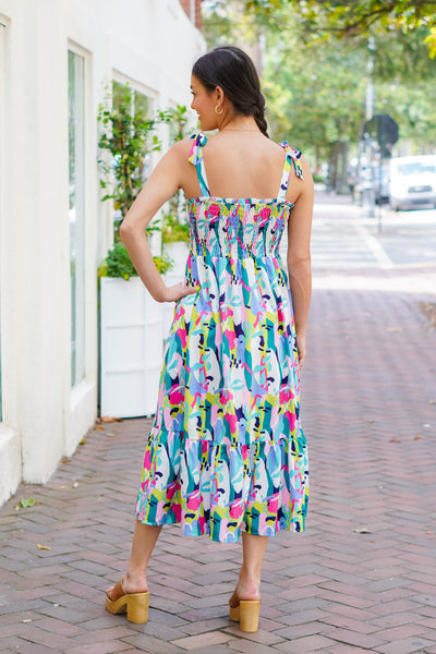 Model is wearing a colorful abstract print midi dress with brown heels on a downtown street.