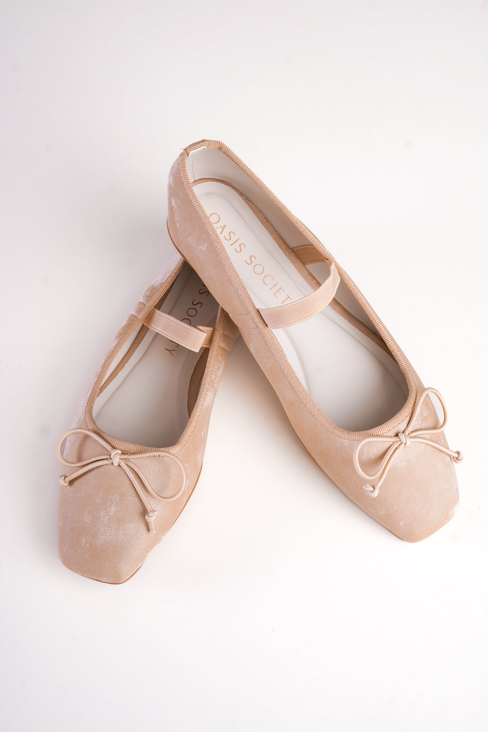 Pair of beige ballet flats with bow details on a white background