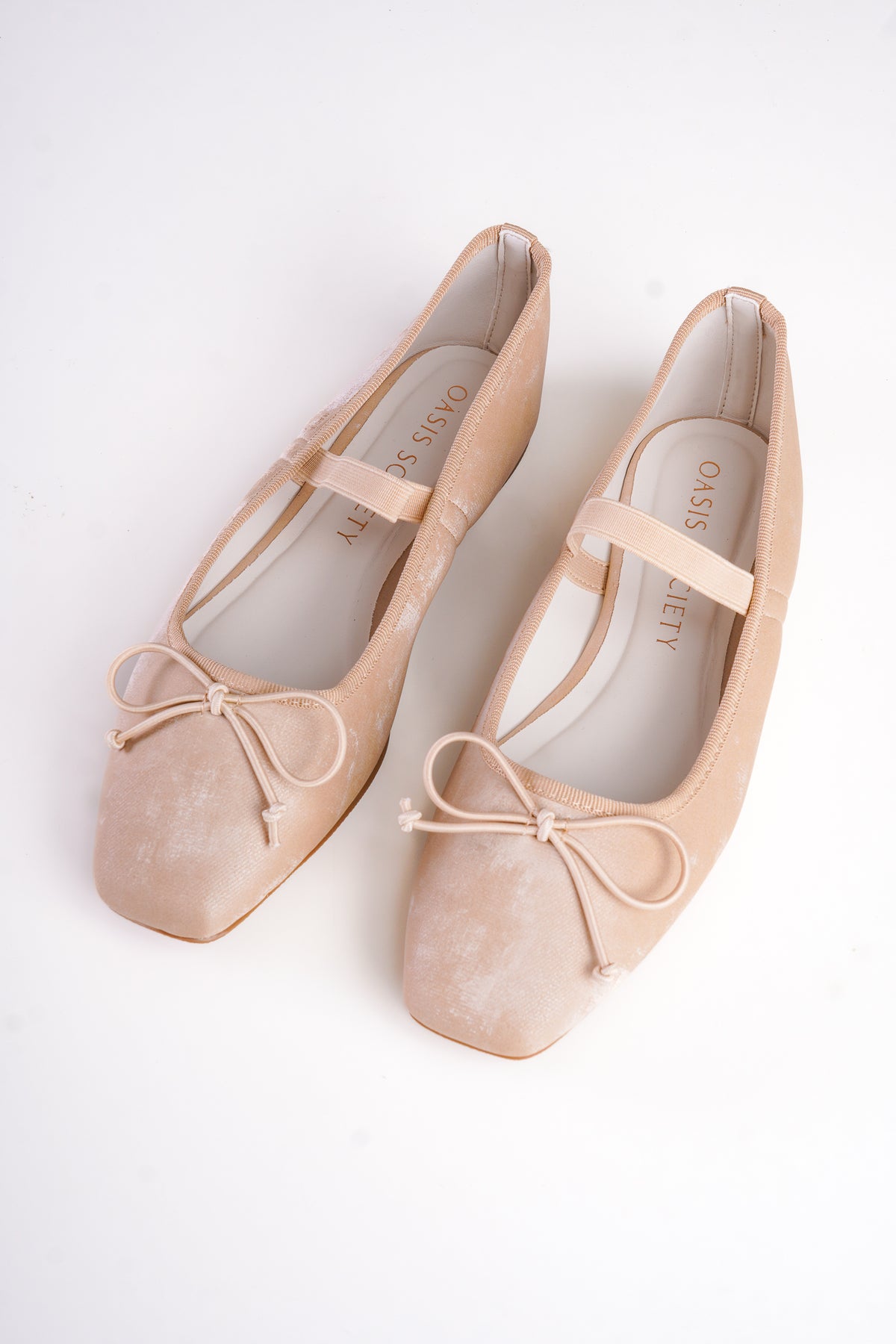 Pair of beige ballet flats with ribbons on a white background