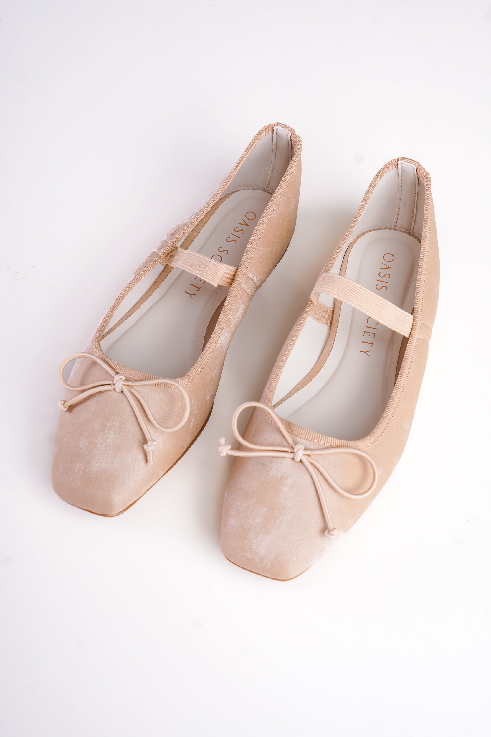 Pair of beige ballet flats with ribbons on a white background