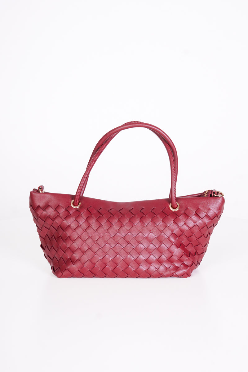 A woven leather handbag in a deep burgundy red, featuring double top handles and gold-tone hardware, photographed against a seamless white background.