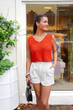 model is wearing a red knit tank with white denim shorts and is holding a black purse