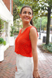 model is wearing a red knit tank with white denim shorts and is holding a black purse