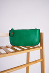 photo shows a green crossbody/ wristlet on a stand