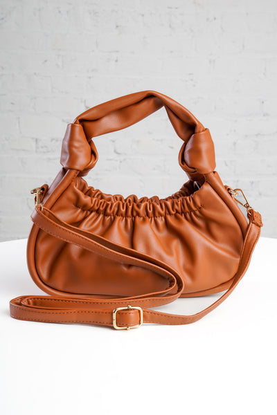 photo shows a green crossbody/ wristlet in front of greenery.