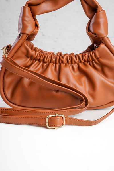photo shows a pink crossbody/ wristlet in front of greenery.