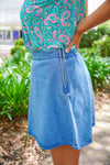 Model is wearing a blue paisley print tank with a blue denim washed skirt in front of greenery.