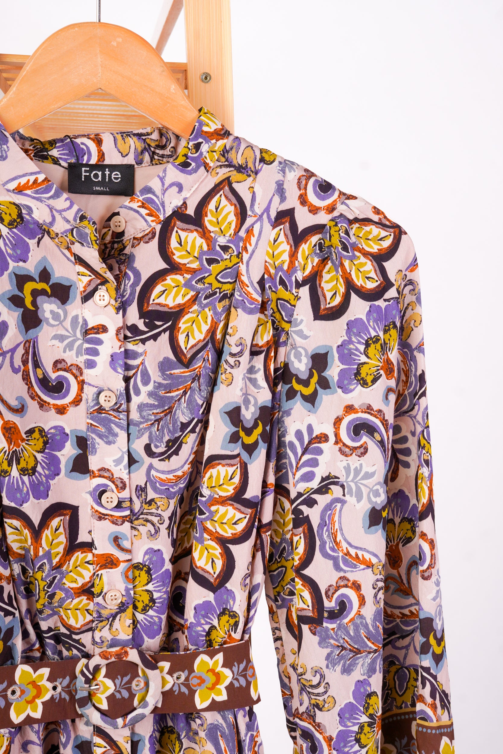 A long-sleeve button-front blouse with a floral and paisley print, hanging on a wooden hanger against a white background. The brand label 'Fate' is visible at the collar.