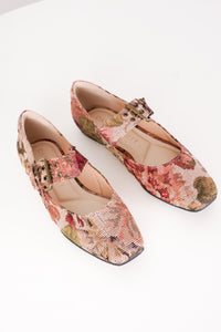 A pair of Mary Jane flats with a textured floral tapestry pattern in muted pink, red, and green tones, featuring a decorative buckle strap and square toes, shown on a white background.
