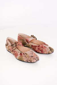A pair of Mary Jane flats with a textured floral tapestry pattern in muted pink, red, and green tones, featuring a decorative buckle strap and square toes, shown on a white background.