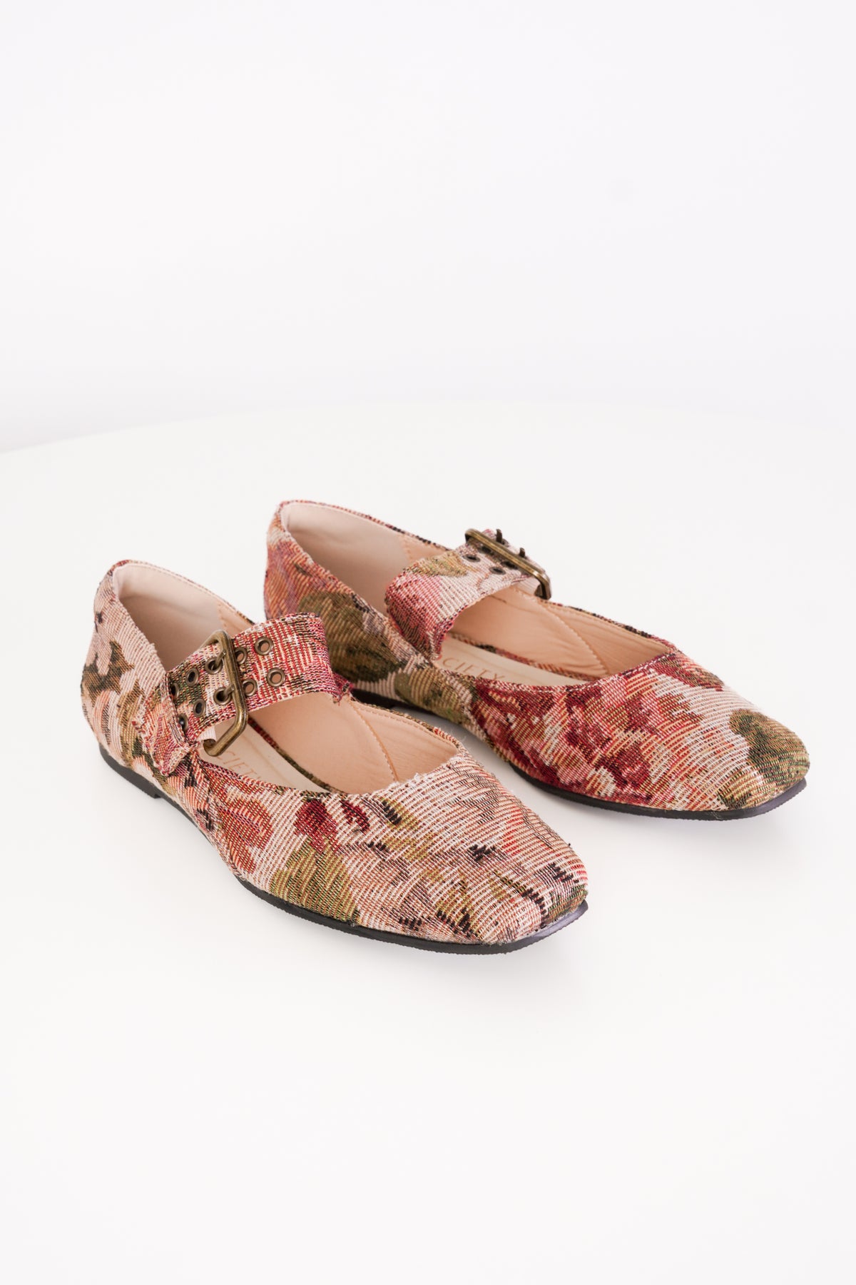A pair of Mary Jane flats with a textured floral tapestry pattern in muted pink, red, and green tones, featuring a decorative buckle strap and square toes, shown on a white background.