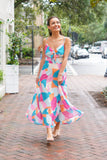 Model is wearing a multicolored midi dress with nude heels on a downtown street.