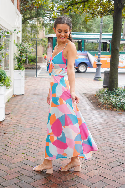Model is wearing a multicolored midi dress with nude heels on a downtown street.