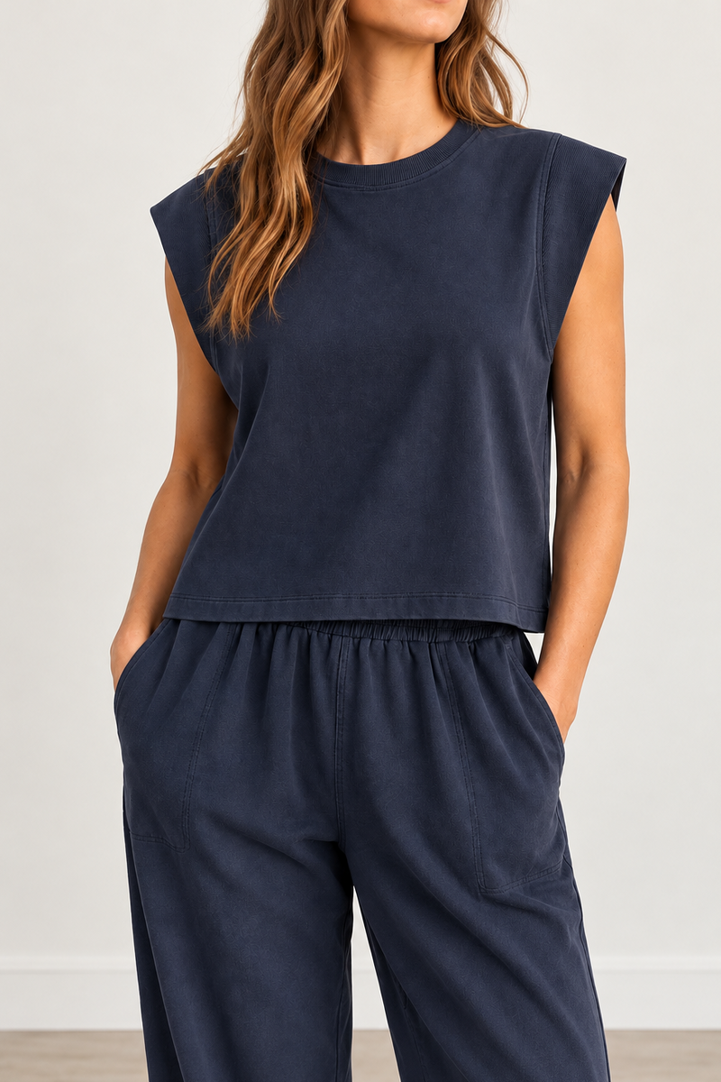 A woman wearing a navy blue sleeveless cropped top and matching wide-leg pants, standing against a light neutral wall.