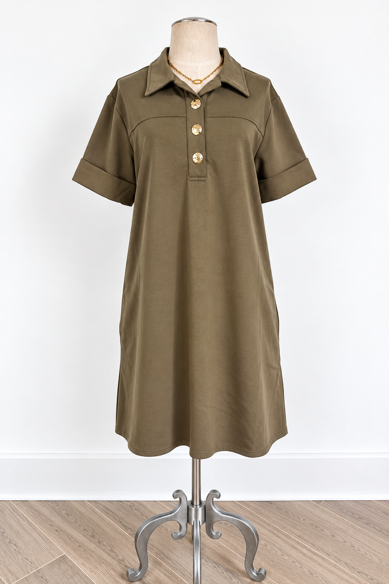 An olive green short-sleeve polo dress displayed on a mannequin stand against a white wall and light wood floor.