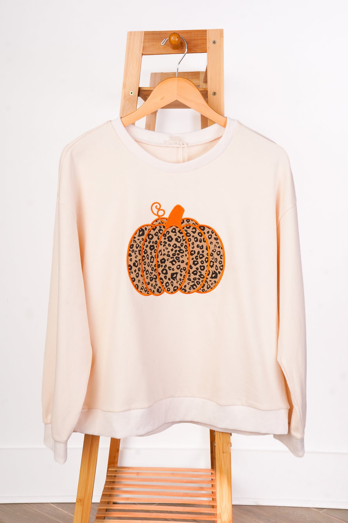 A cream-colored crewneck sweatshirt with a leopard-print pumpkin graphic on the front