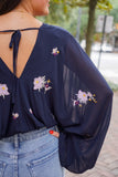 Model is wearing a navy, sheer, cropped top with long sleeves and small embroidered flowers on the top