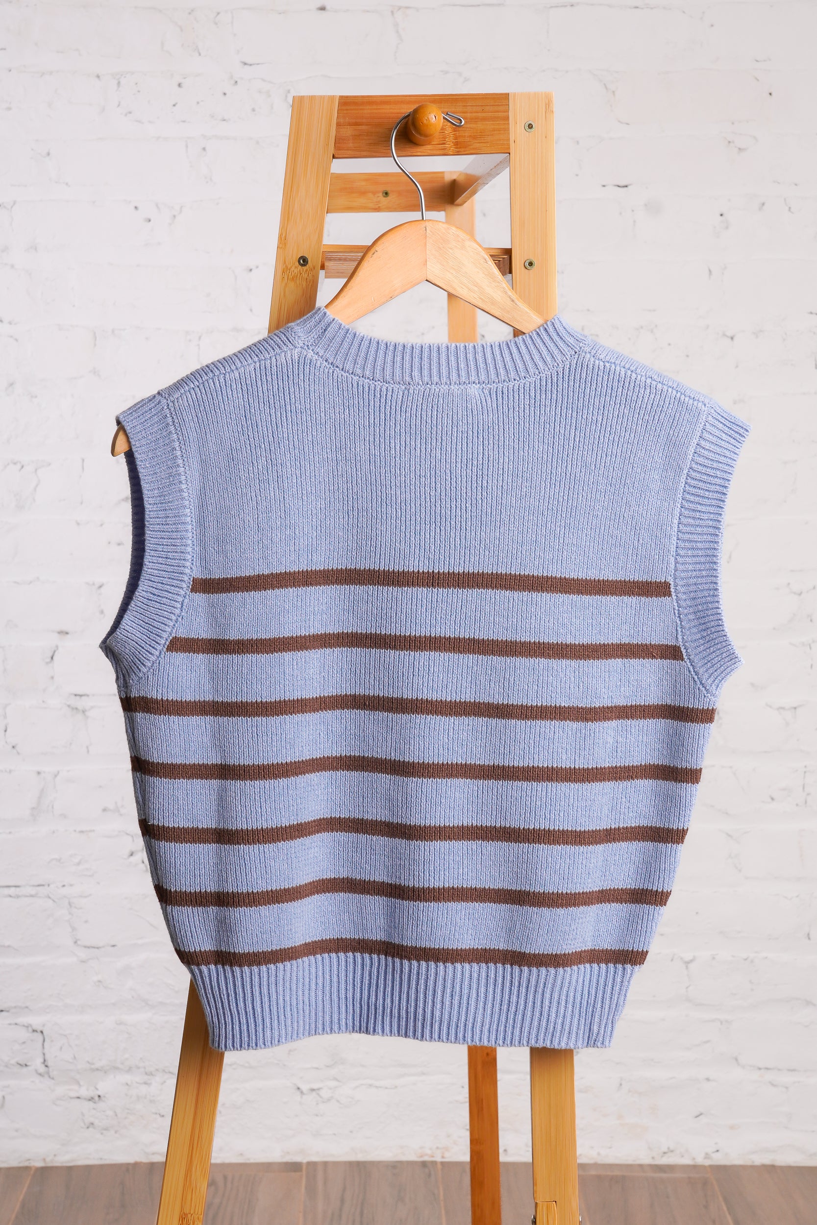 Sleeveless, crew neck, sky blue sweater vest with brown horizontal stripes. 