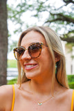 Model is wearing tortoise print sunglasses with a yellow dress and green earrings on.
