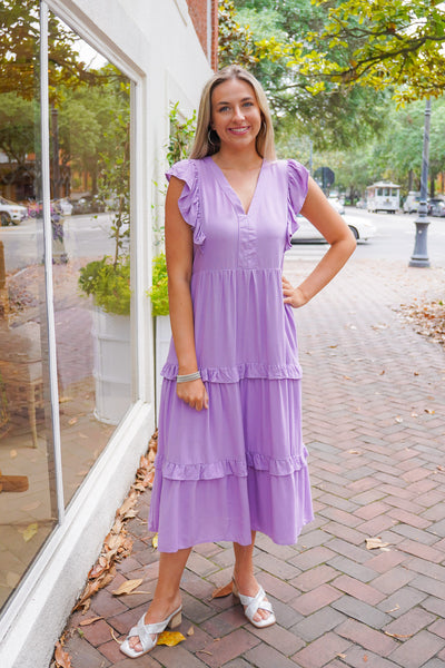model is wearing a purple midi dress with silver heels on a downtown street.