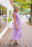 model is wearing a purple midi dress with silver heels on a downtown street.
