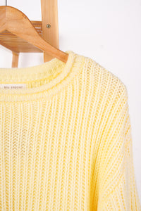 A pale yellow chunky knit sweater hanging on a wooden hanger against a plain white background.
