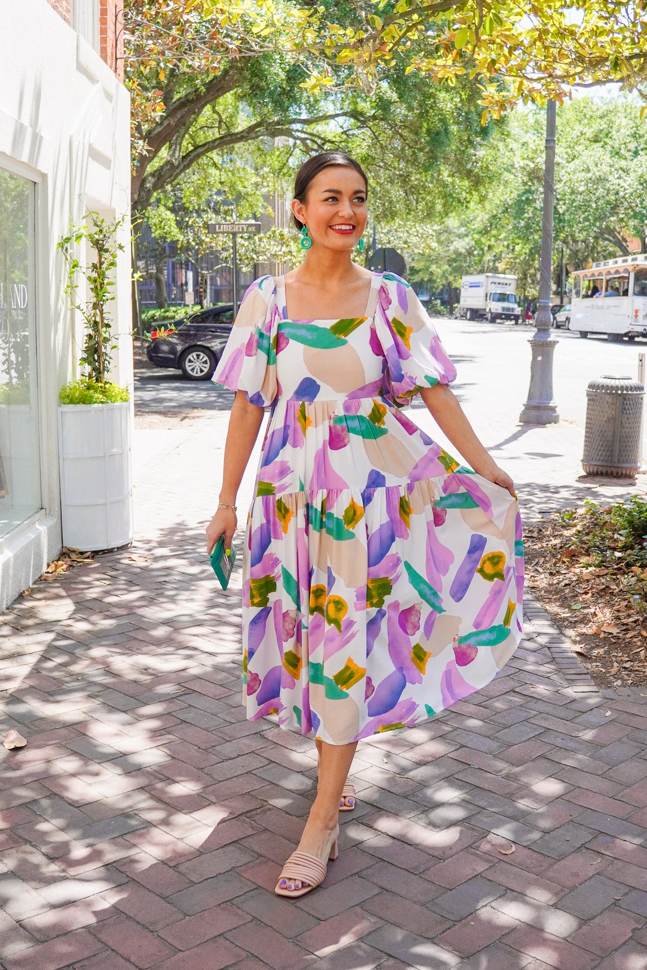 Model is wearing a colorful midi dress with puff sleeves paired with nude heels and green earrings