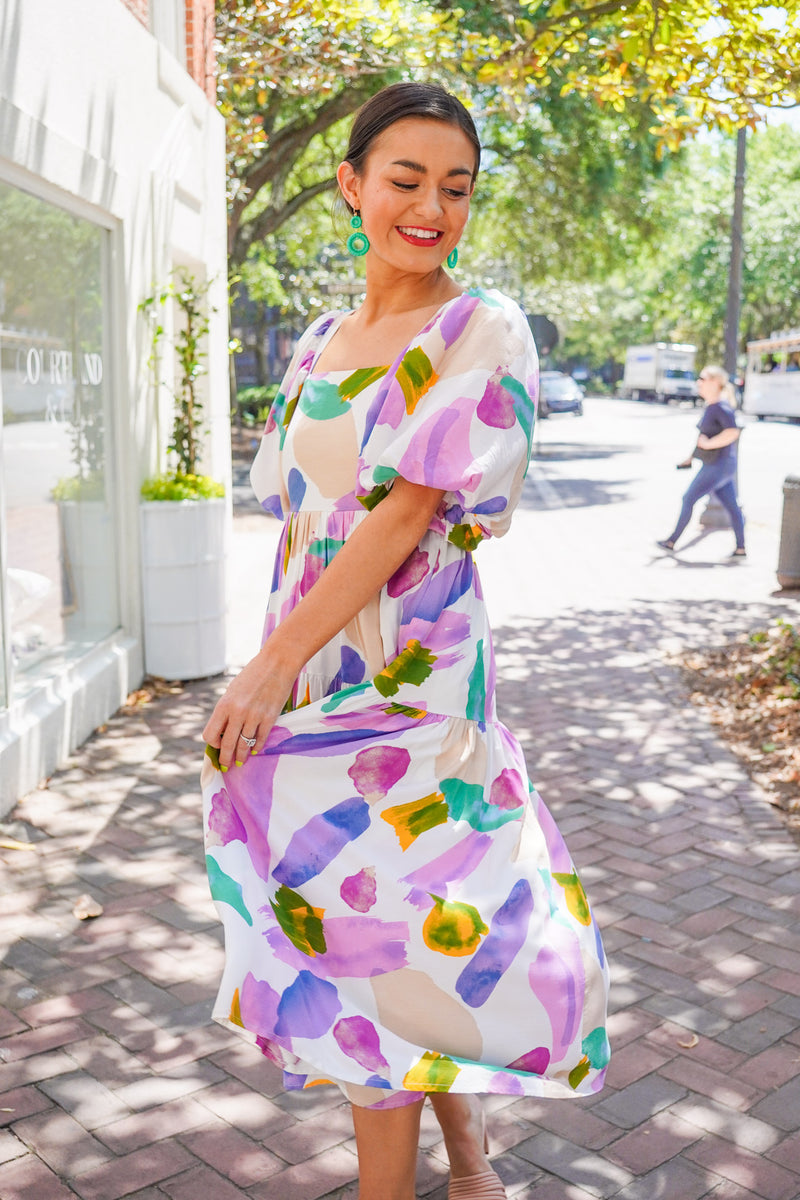 Model is wearing a colorful midi dress with puff sleeves paired with nude heels and green earrings