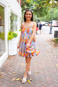 Model is wearing a multi color, spaghetti strapped, mini dress in front of downtown landscape.