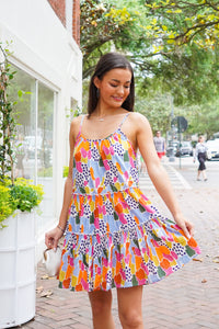 Model is wearing a multi color, spaghetti strapped, mini dress in front of downtown landscape.