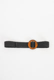 A black woven belt that has a small leather flap on the end and a brown wooden circle for the buckle closure. 