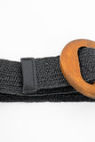 A close up picture to show the details of a black woven belt with a brown circle buckle. 
