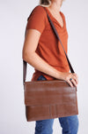 Model is wearing a rust colored tee shirt with a pair of straight leg denim. She is carrying a brown over the shoulder bag with a flap closure and white contrast stitching on brown faux leather. 
