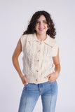 Model is wearing a Cream colored, cable knit sweater vest with a pair of straight leg, seam front denim. 