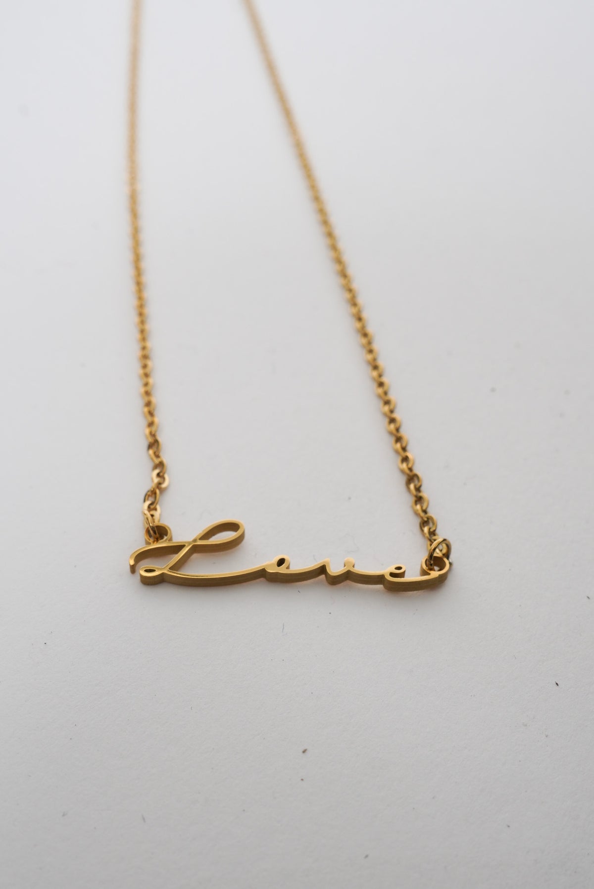 A dainty gold necklace with the word "love" written in a script font. 