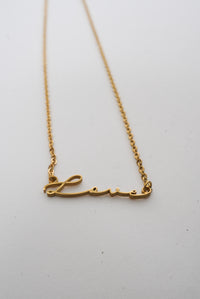 A dainty gold necklace with the word "love" written in a script font. 