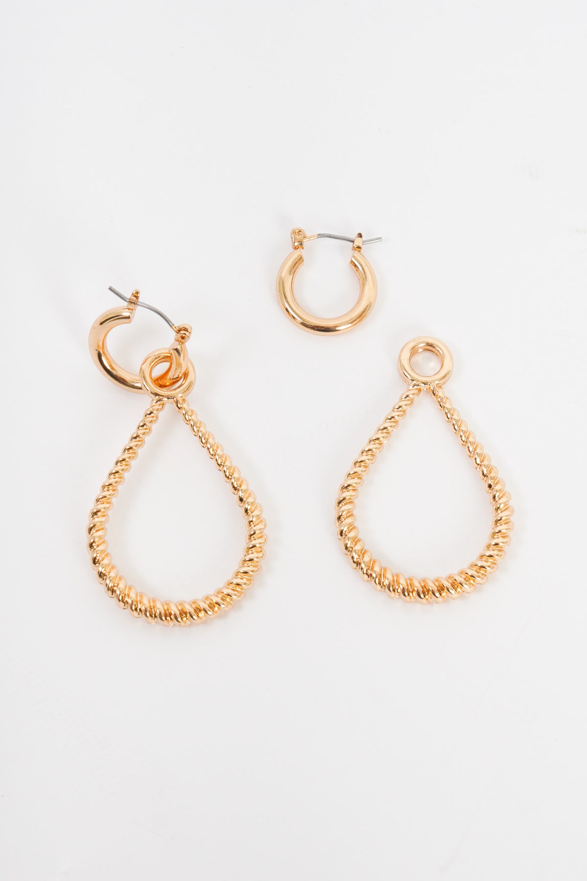 A pair of earrings that feature a unique two in one deal. The earrings are made up of a small gold hoop that has a small clasp for the closure. On the small hoop is a twisted teardrop earring that can be worn with the small hoop, or you can wear the small hoop by itself. The teardrop earring has a small circle that allows you to slide it on and off of the small hoop. 