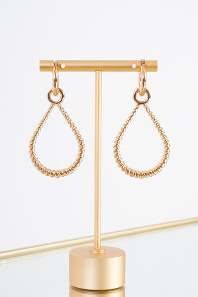 A pair of gold earrings that are showcased on a gold earring stand. The earrings feature a a small gold hoop with an attachable twisted teardrop earring. The small hoop has a clasp backing. 
