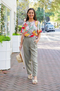 model is wearing olive green, linen pants with a floral top and gold sandals