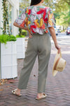 model is wearing olive green, linen pants with a floral top and gold sandals