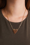 Photo shows a heart shaped charm attached to a dainty gold chain. 
