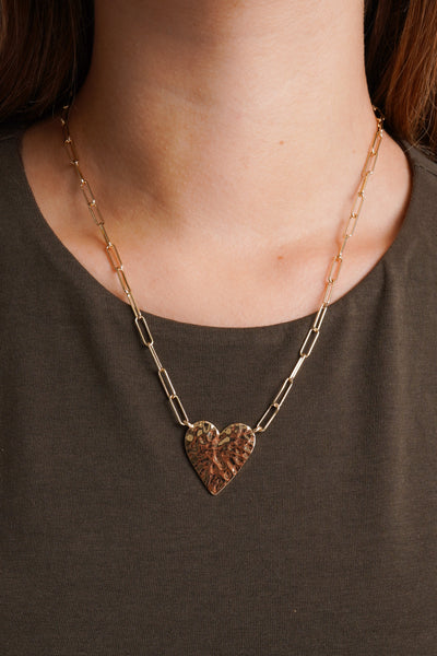 Photo shows a heart shaped charm attached to a dainty gold chain. 