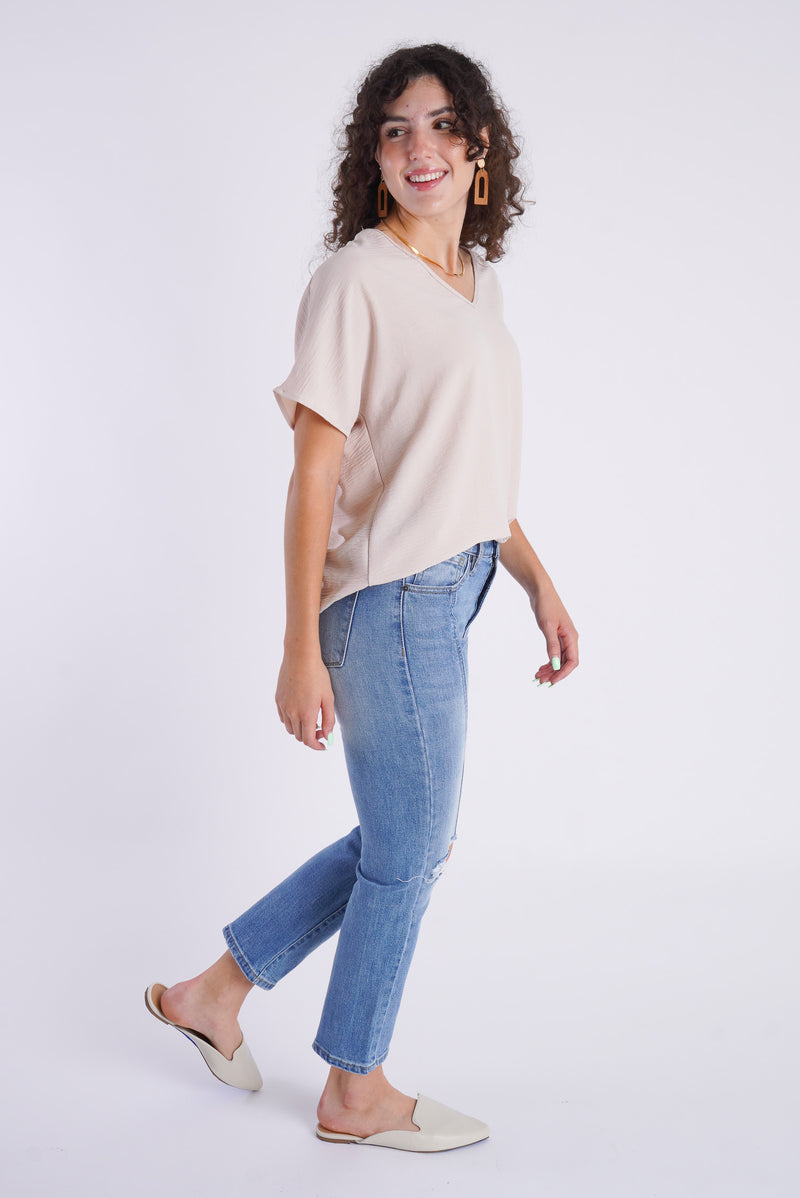 A side view of a model wearing a champagne colored top and medium wash, slim straight denim. 