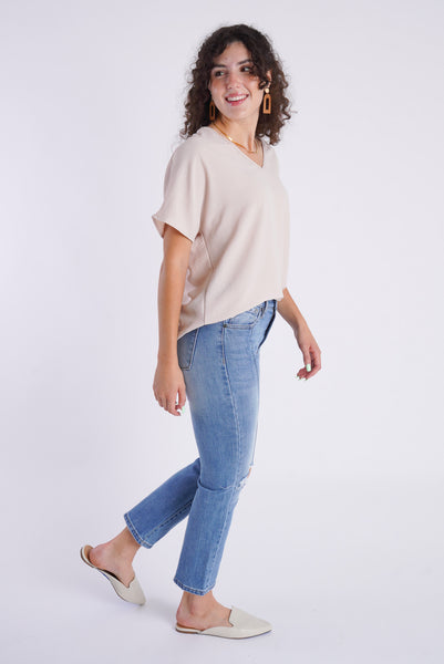 A side view of a model wearing a champagne colored top and medium wash, slim straight denim. 