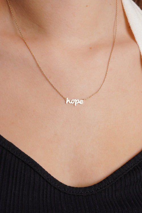 Photo shows an up close photo of a dainty necklace with a charm with the word "hope". 